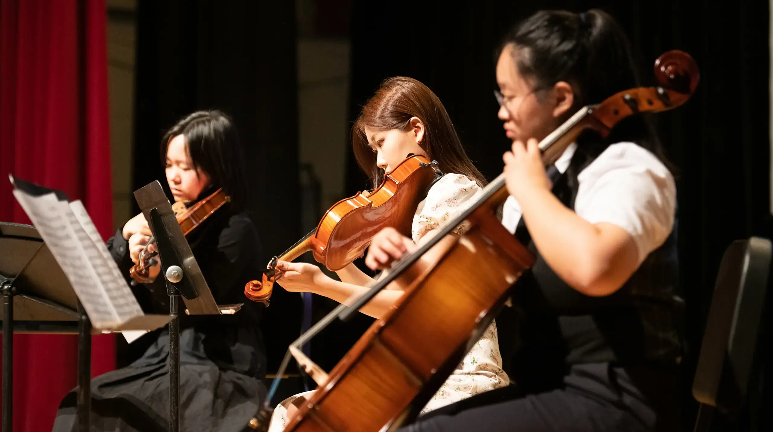 Three female students playing string instruments.